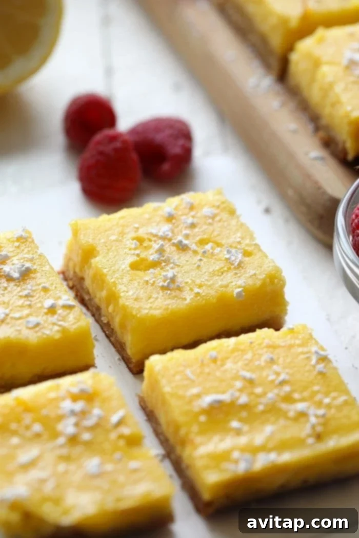 Four perfectly portioned gluten-free lemon bars garnished with fresh raspberries, ready to be enjoyed.