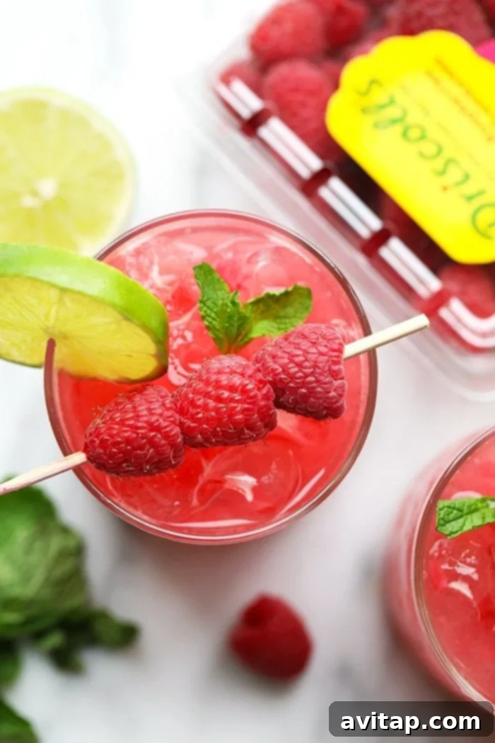 Two glasses of Raspberry Ginger Mojito, garnished with lime and mint, on a wooden surface.