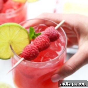 A person holding a raspberry mojito garnished with lime.