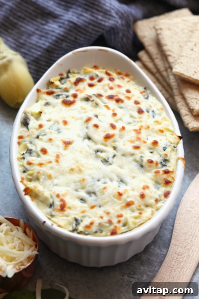 Enjoy this AMAZING lightened-up, restaurant-style Healthy Spinach and Artichoke Dip for a nutrition-packed snack or appetizer all year round. This spinach and artichoke dip will quickly become a crowd-pleasing recipe you'll make again and again. A large bowl of lightened-up spinach artichoke dip, garnished and ready for serving at a party.