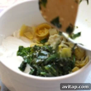 Bubbly Baked Spinach Artichoke Delight 3 a bowl full of greens and cheese in a white bowl, Lightened Up Spinach and Artichoke Dip.
