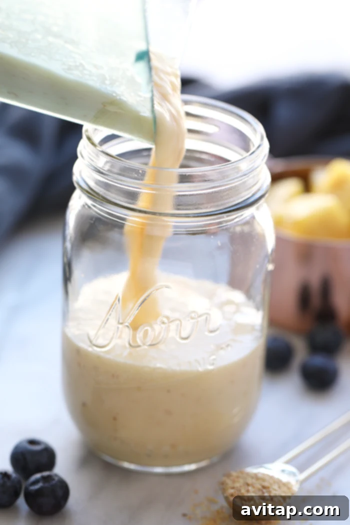 A hand pouring a vibrant yellow ginger pineapple smoothie from a blender into a tall glass, showcasing its smooth and creamy texture.