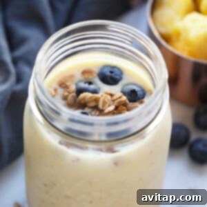 Breakfast in a jar with blueberries and granola, accompanied by a ginger pineapple smoothie, ready to be enjoyed.