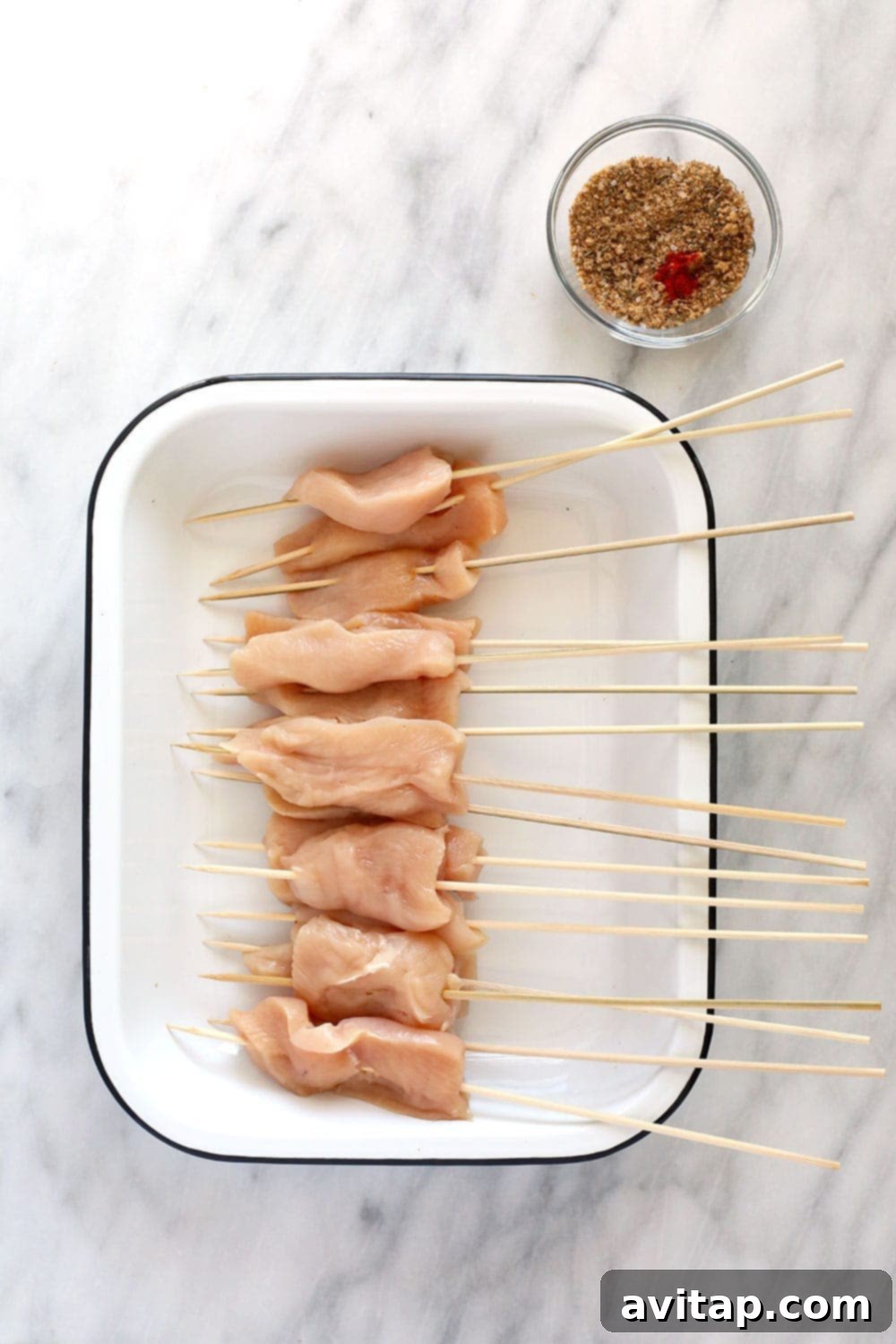 Raw chicken breast strips meticulously threaded onto wooden skewers, ready for seasoning.