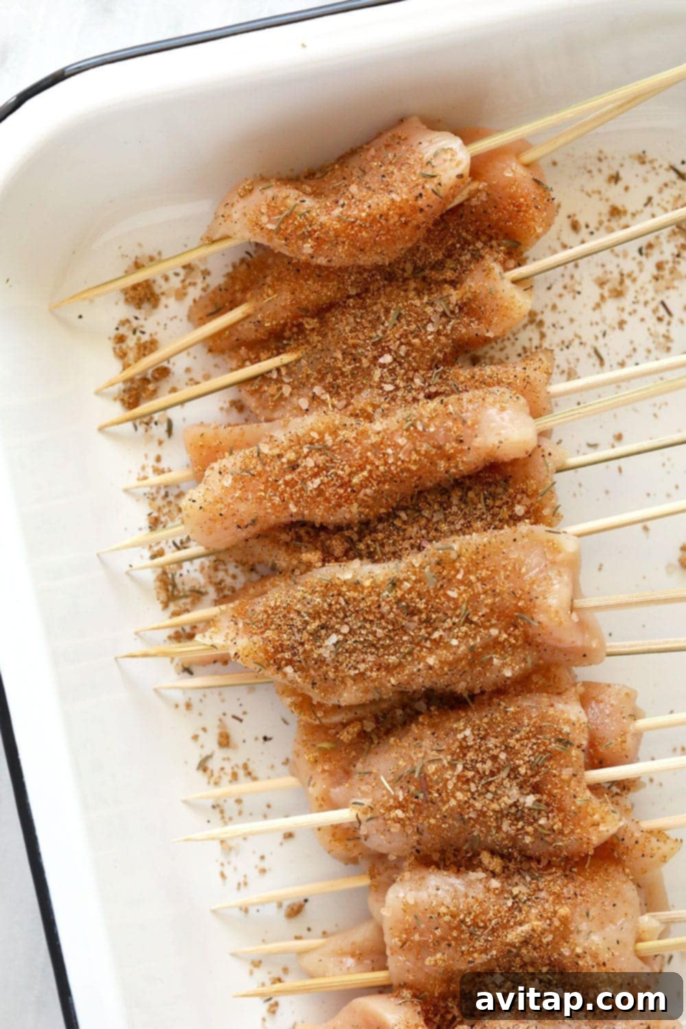 Raw chicken breast strips coated generously with dry rub spices, laid out on a tray.
