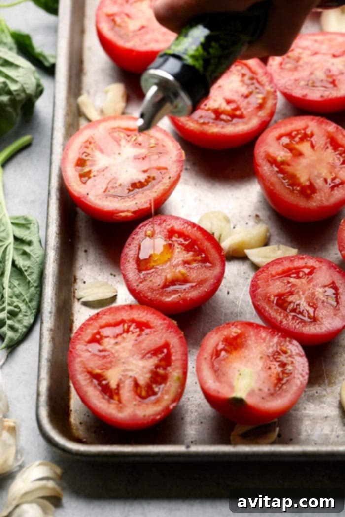 Make your own homemade roasted tomato sauce using fresh, juicy tomatoes from the garden! Roast your tomatoes and puree them with garlic cloves, olive oil, and fresh basil. Juicy tomatoes and garlic cloves on a baking pan, ready for roasting.