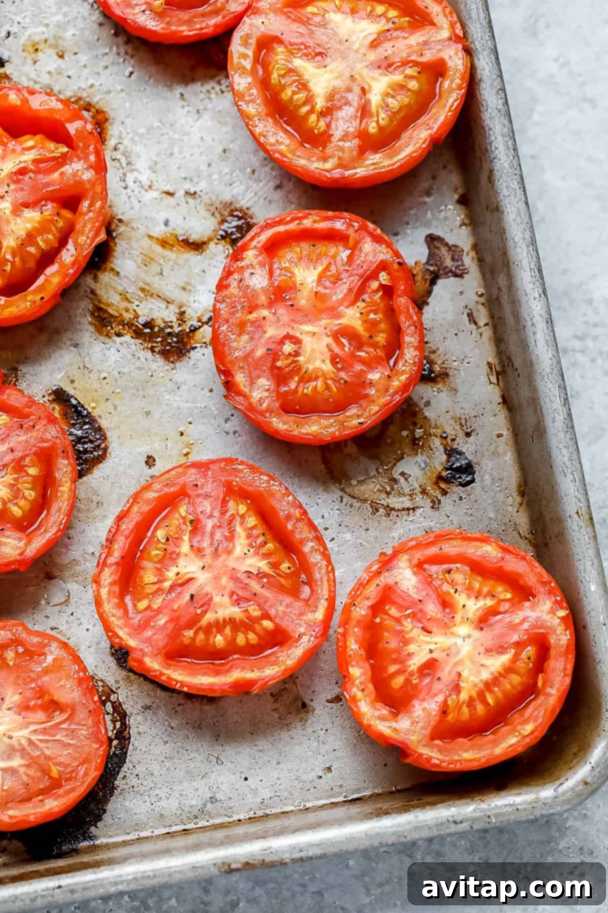 Make your own homemade tomato sauce using fresh, juicy tomatoes from the garden! Roast your tomatoes and puree them with garlic cloves, olive oil, and fresh basil. Roasted tomatoes on a baking sheet, golden and tender.