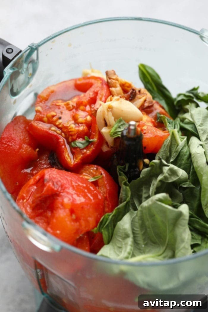 Make your own homemade roasted tomato sauce using fresh, juicy tomatoes from the garden! Roast your tomatoes and puree them with garlic cloves, olive oil, and fresh basil. Roasted tomatoes, garlic, and fresh basil in a food processor, ready for blending.