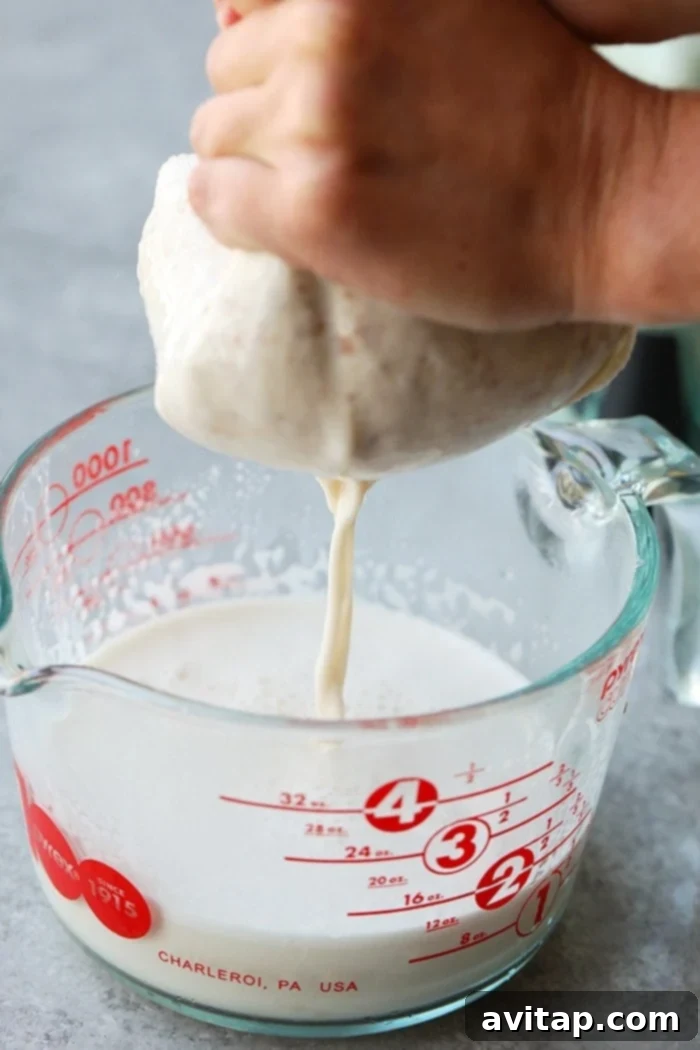 Freshly blended almond milk being strained through a nut milk bag held over a large bowl, revealing creamy white milk.