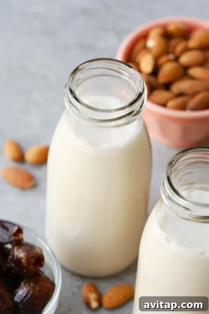 A glass jug filled with homemade almond milk, garnished with a vanilla bean pod, on a rustic wooden surface.