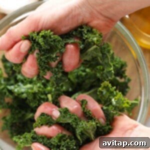 Close-up of hands massaging kale leaves in a bowl with olive oil and salt.