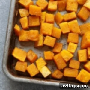 Close-up of butternut squash cubes seasoned with olive oil, salt, and pepper on a baking sheet, ready for roasting.