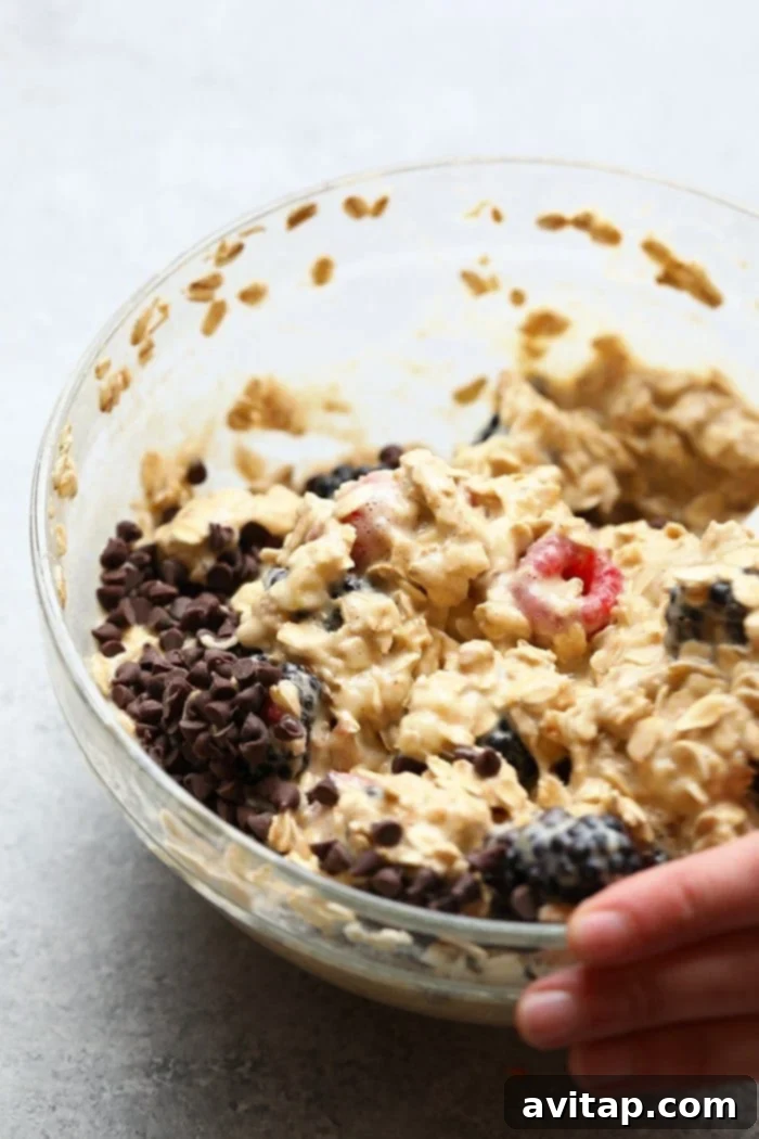 An individual serving of baked oatmeal in a white bowl, generously topped with fresh berries and a drizzle of maple syrup