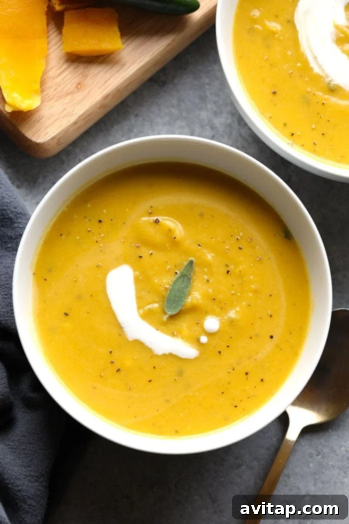 Two bowls of creamy spicy butternut squash soup garnished with fresh sage leaves and a drizzle of coconut cream.