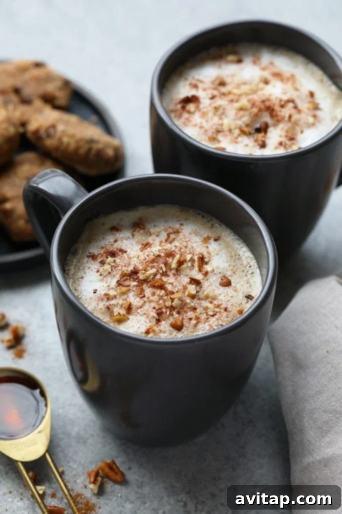 Two mugs of homemade maple pecan latte, topped with whipped cream, chopped pecans, and a sprinkle of cinnamon, against a cozy backdrop.