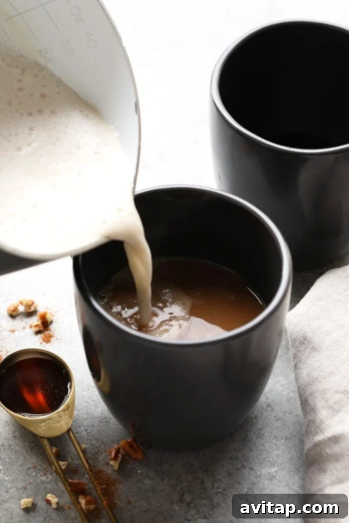 A close-up of a homemade maple pecan latte, showing the frothy top, pecans, and cinnamon, in a black mug.