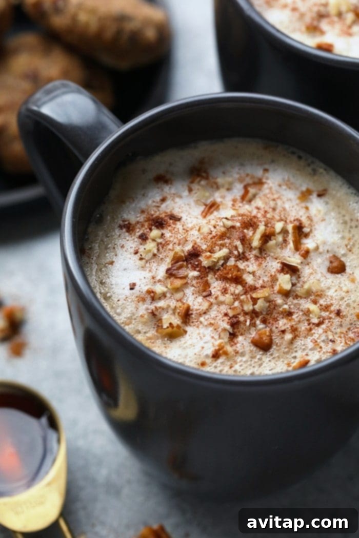 A person's hand holding a mug of maple pecan latte, with a cozy sweater and a book in the background, depicting a relaxing moment.