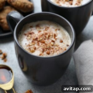 DIY maple pecan latte with whipped cream and pecans served in two black mugs.