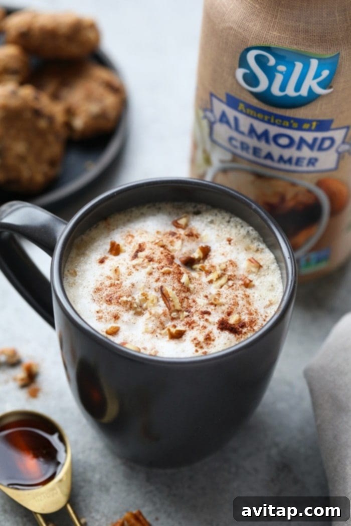 A top-down view of a steaming maple pecan latte in a white mug, garnished with a generous swirl of whipped topping, crunchy pecans, and a dusting of cinnamon, inviting a moment of warmth and comfort.
