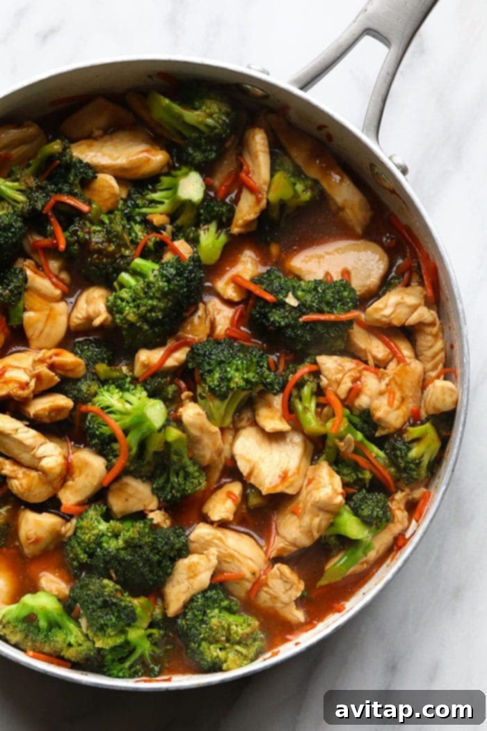 Close-up of chicken and crisp vegetables sizzling in a large stir-fry pan, coated in a glossy, rich sauce.