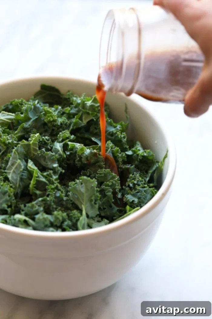 Massaged kale in a bowl with rich, red pomegranate salad dressing being poured over, illustrating the key step in preparation