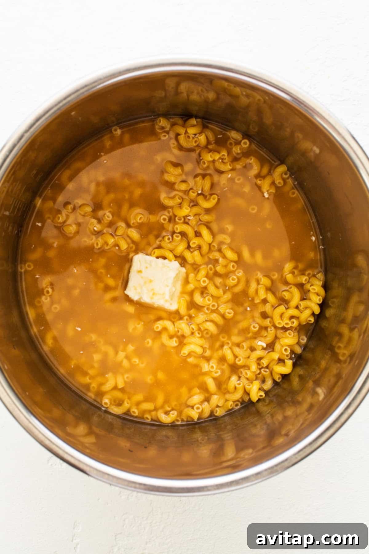 Made with 17g of protein and completely in your Instant Pot, this Protein Mac and Cheese is delicious, creamy, and easy to make! Uncooked elbow noodles, a stick of butter, and chicken broth in the Instant Pot liner, ready for cooking.