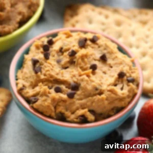 A bowl of peanut butter hummus with strawberries and crackers, topped with edible cookie dough.