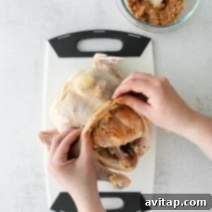 A person's hands sprinkling spices on a raw chicken to prepare beer can chicken.