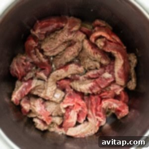 Close-up of seared beef strips cooking in the Instant Pot, showing the browning process for flavor development.