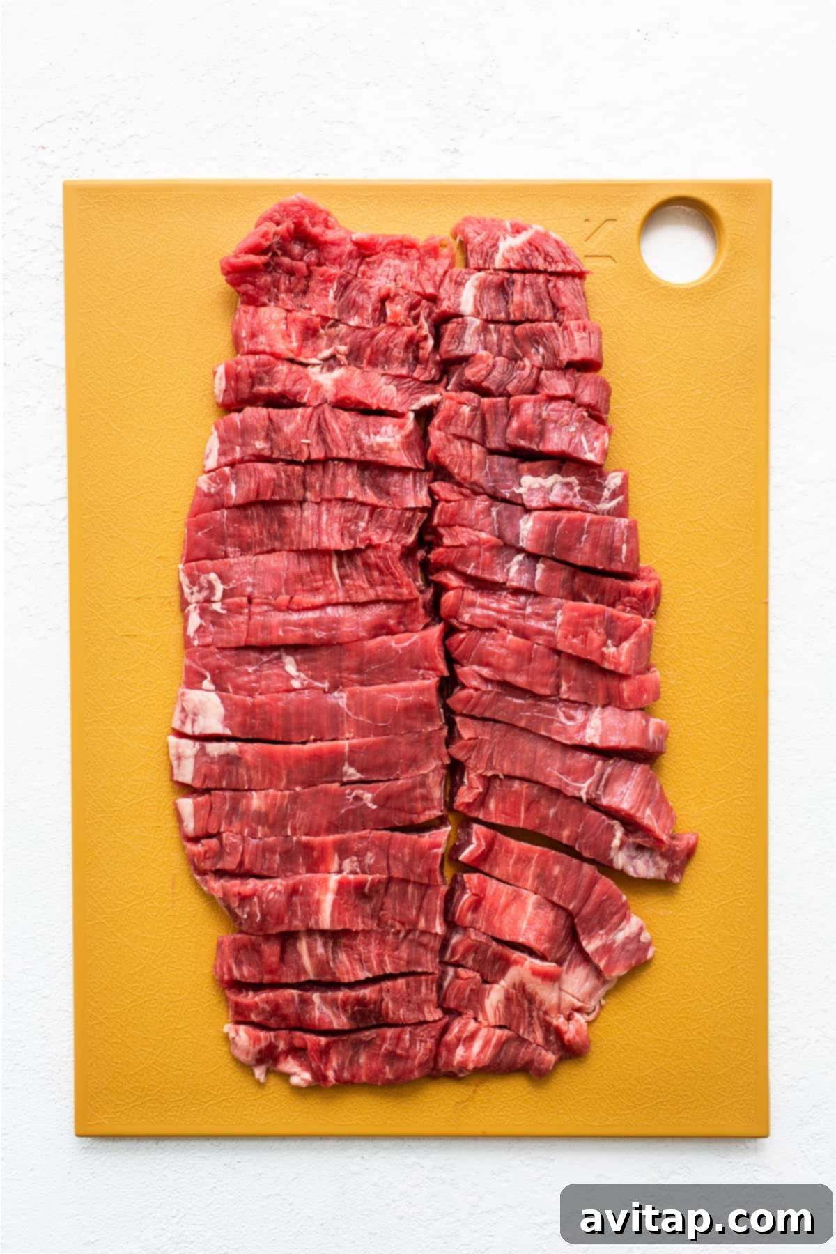 Perfectly sliced flank steak on a wooden cutting board, prepped and ready for cooking in Instant Pot Beef and Broccoli.