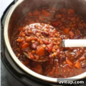 A close-up shot of steaming Instant Pot chili in a rustic bowl, showcasing its rich texture and hearty ingredients with visible lentils, beans, and vegetables.