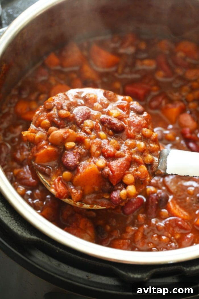 A ladle serving steaming Instant Pot Vegan Chili directly from the pressure cooker, showcasing its hearty texture and indicating it's ready to be portioned out.