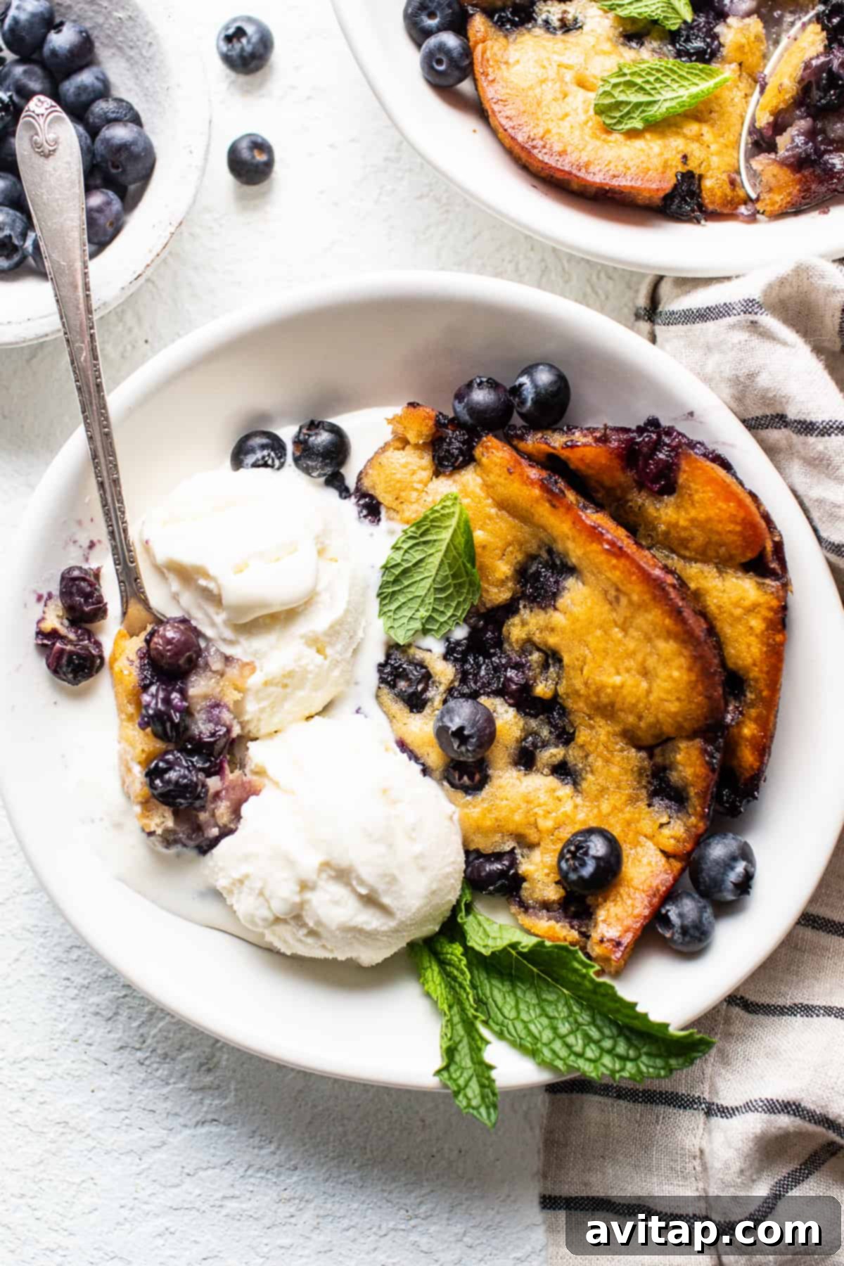 A bowl of freshly baked blueberry cobbler, richly golden on top, served with a generous scoop of melting vanilla ice cream, creating a delightful contrast of warm and cold.