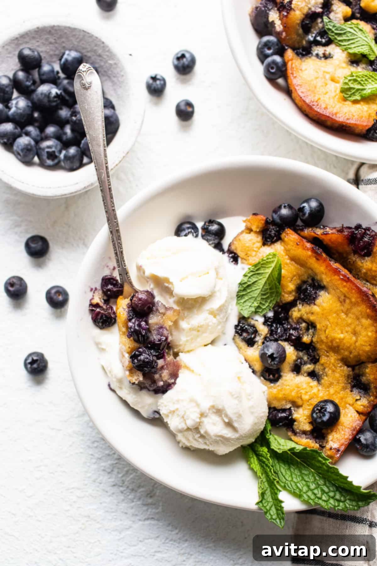 A close-up of a serving of warm blueberry cobbler in a white bowl, generously topped with melting vanilla ice cream, highlighting its inviting texture.