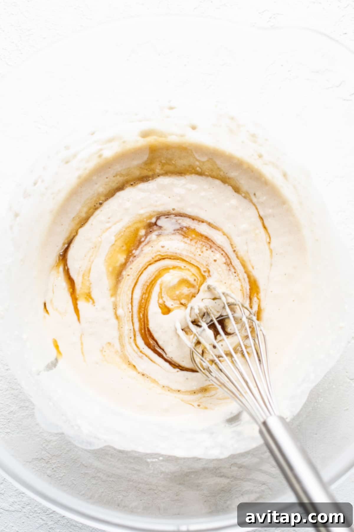 A mixing bowl filled with a smooth, light-colored cobbler topping batter, ready to be combined with the juicy blueberries.