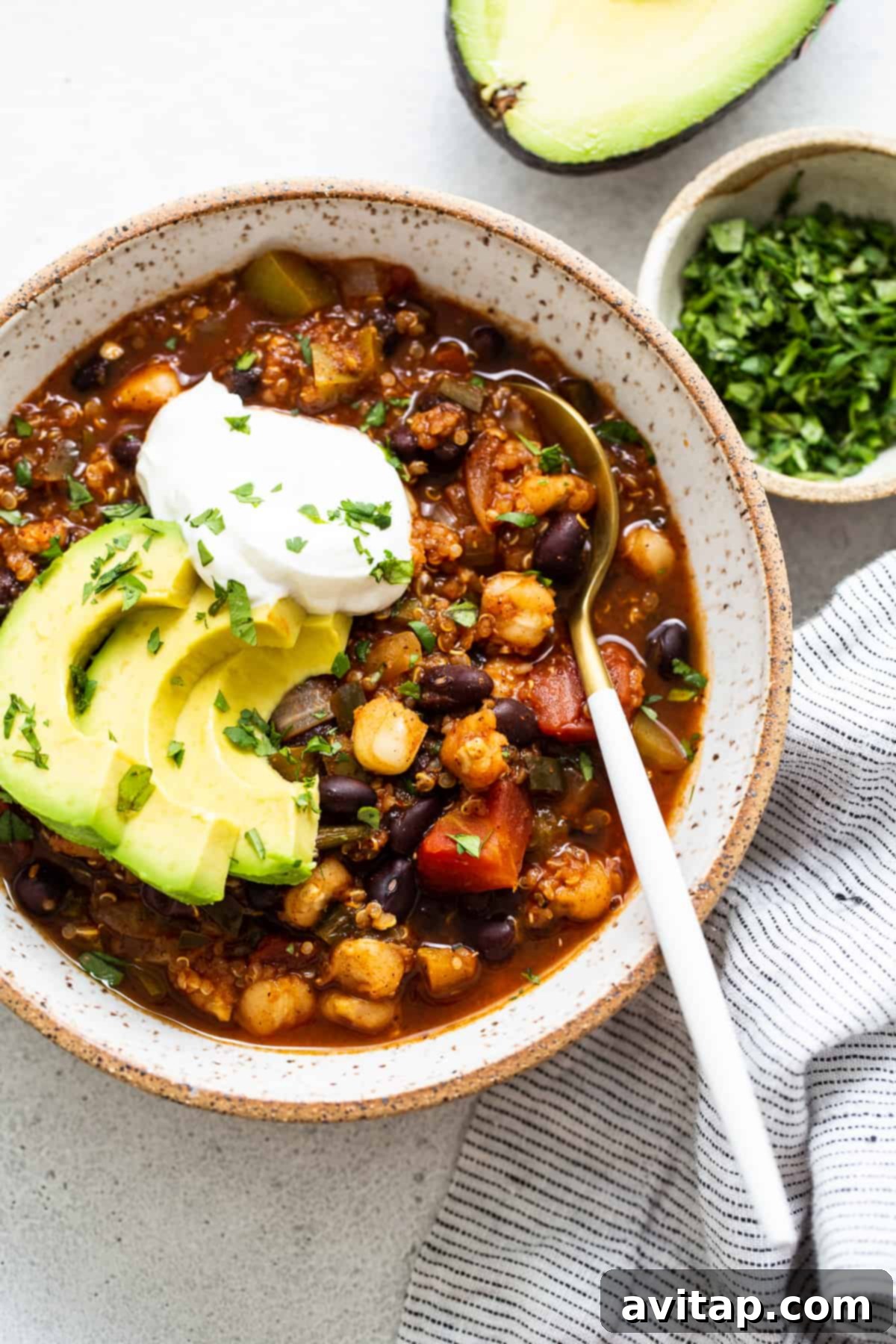 A vibrant bowl of black bean quinoa chili, generously topped with creamy avocado and a dollop of sour cream, ready to be enjoyed.