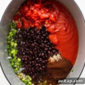 All the ingredients for black bean quinoa chili, including beans, tomatoes, hominy, and spices, are combined in a Dutch oven and stirred before simmering.