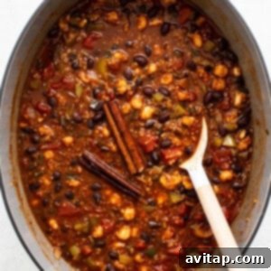 Cooked quinoa chili, thick and hearty, in a Dutch oven after simmering, with a spoon stirring the mixture.