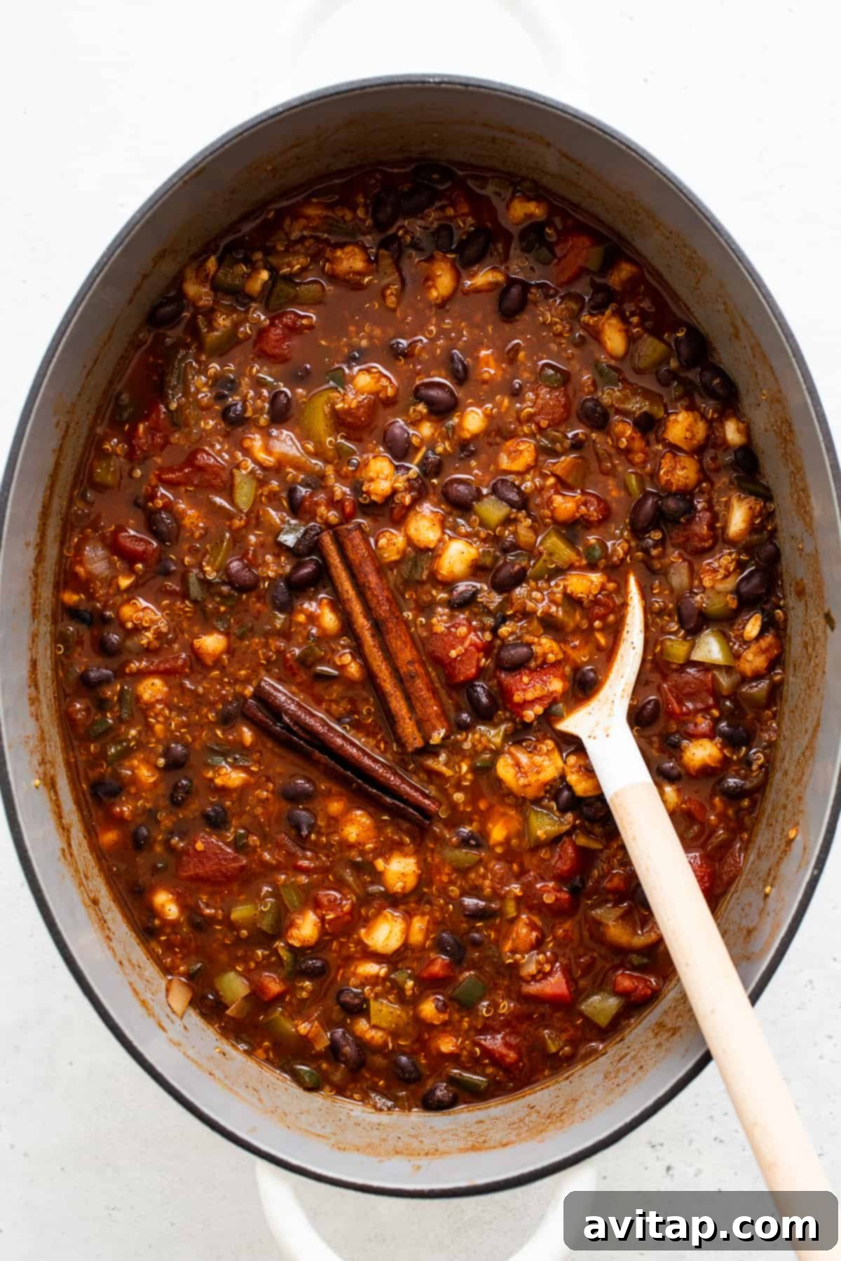 Close-up of black bean quinoa chili simmering gently in a Dutch oven on the stovetop, steam rising from the richly textured surface.