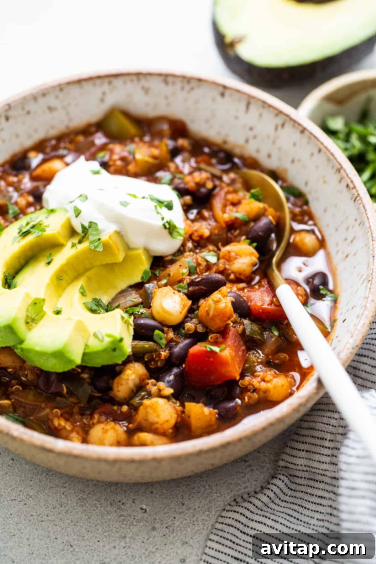 A beautifully presented bowl of black bean quinoa chili, garnished with fresh cilantro, creamy avocado slices, and a dollop of sour cream, ready to be served.