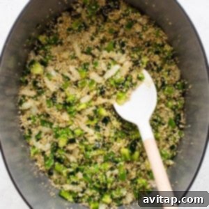 Chopped onions, peppers, and uncooked quinoa sautéing in olive oil in a Dutch oven on the stovetop.