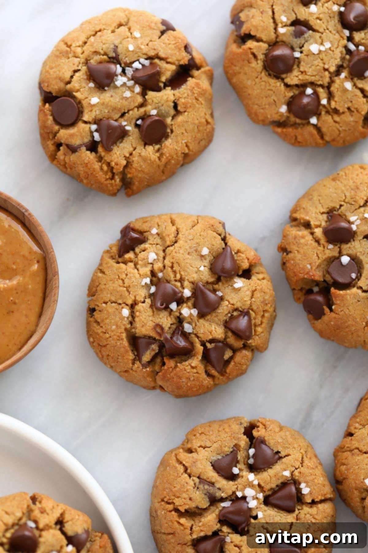 Close-up of a healthy peanut butter cookie, topped with abundant dark chocolate chips and coarse sea salt, showcasing its inviting texture.