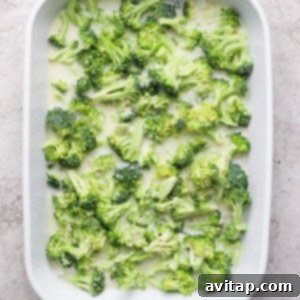A white baking dish filled with fresh broccoli florets on a light textured background.