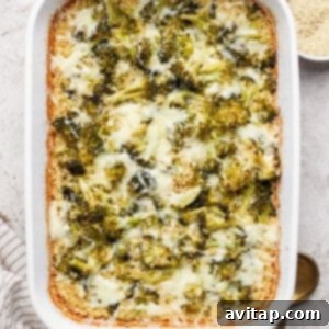 A baked casserole in a white dish with melted cheese and broccoli, accompanied by bowls of grated cheese and breadcrumbs. A striped towel and two spoons are nearby.