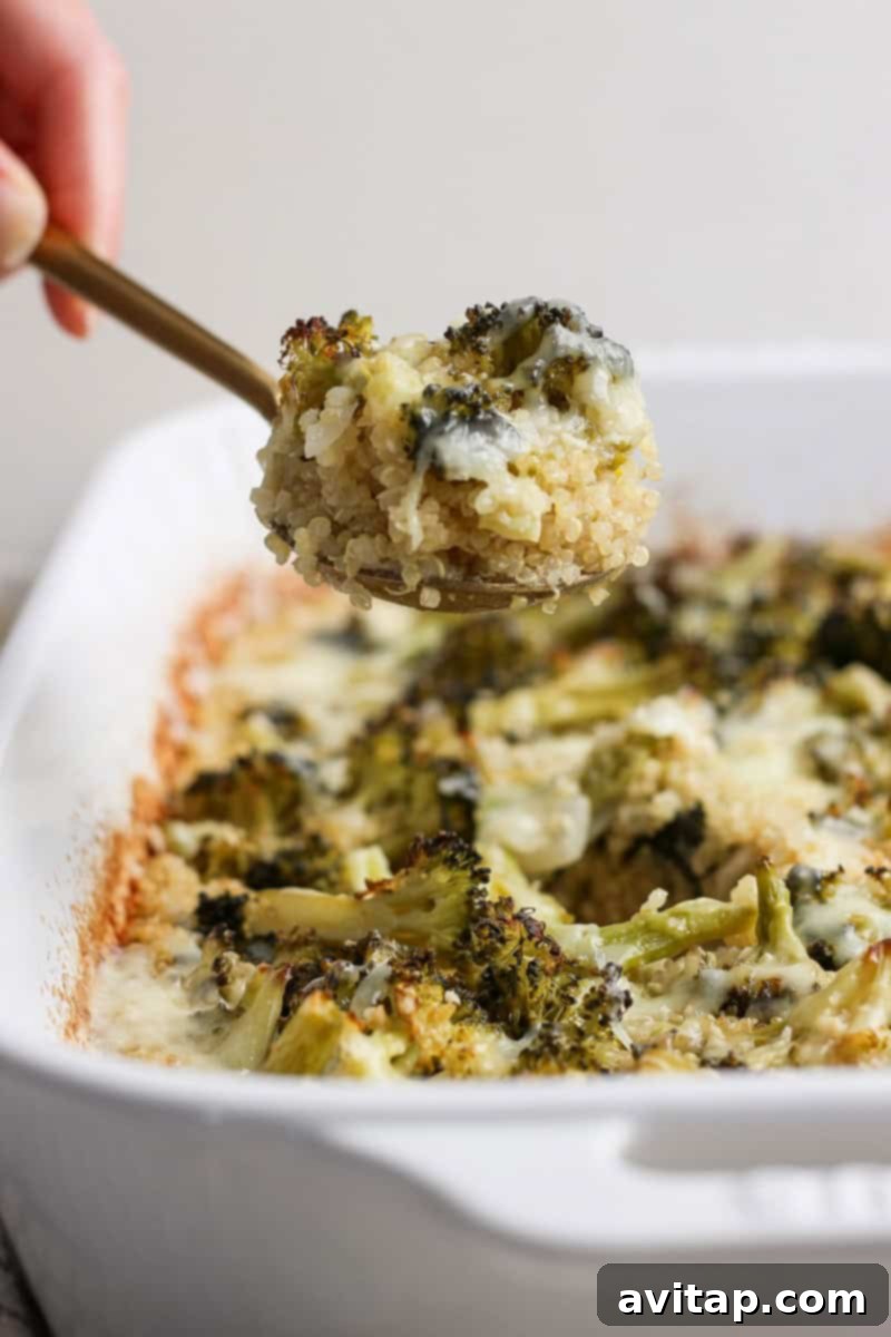 A spoon scooping a portion of baked quinoa and broccoli from a white dish.