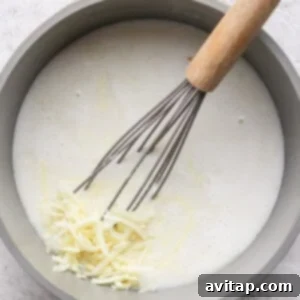 A pot containing a creamy liquid mixture with shredded cheese being whisked in.