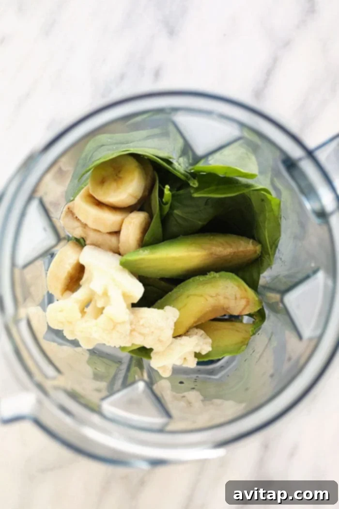 Various green smoothie ingredients including spinach, banana, avocado, and almond milk laid out near a blender.