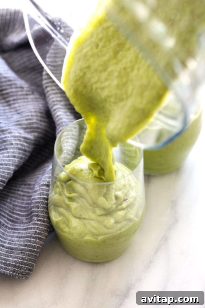 A stream of vibrant green smoothie pouring from a blender into a tall glass, indicating freshness and readiness.