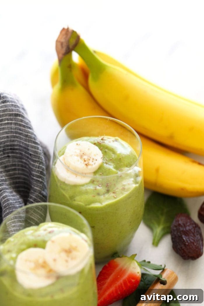 Two green smoothies, beautifully garnished with fresh banana slices and a sprinkle of flax seeds, sitting on a countertop.