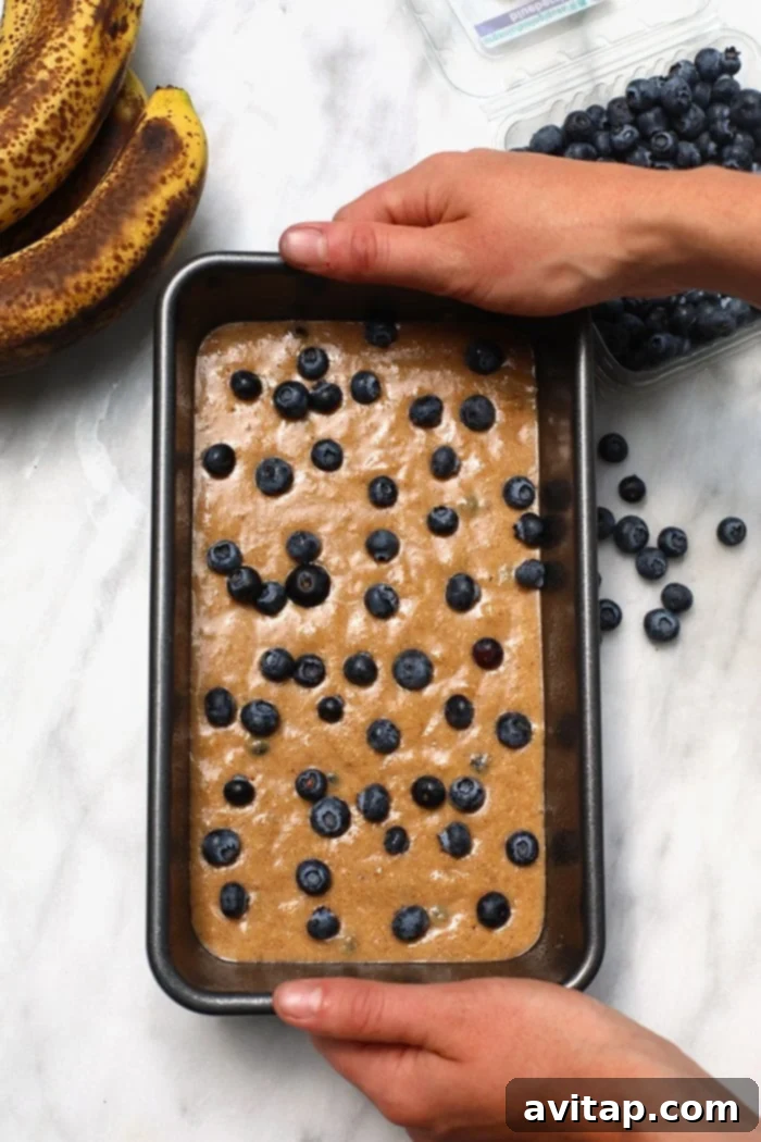 This healthy blueberry banana bread is an easy breakfast that the whole family will love! It is naturally sweetened, delicious and you just can’t beat moist banana bread. Make a loaf today! Banana bread batter being poured into a greased loaf pan, ready for baking.